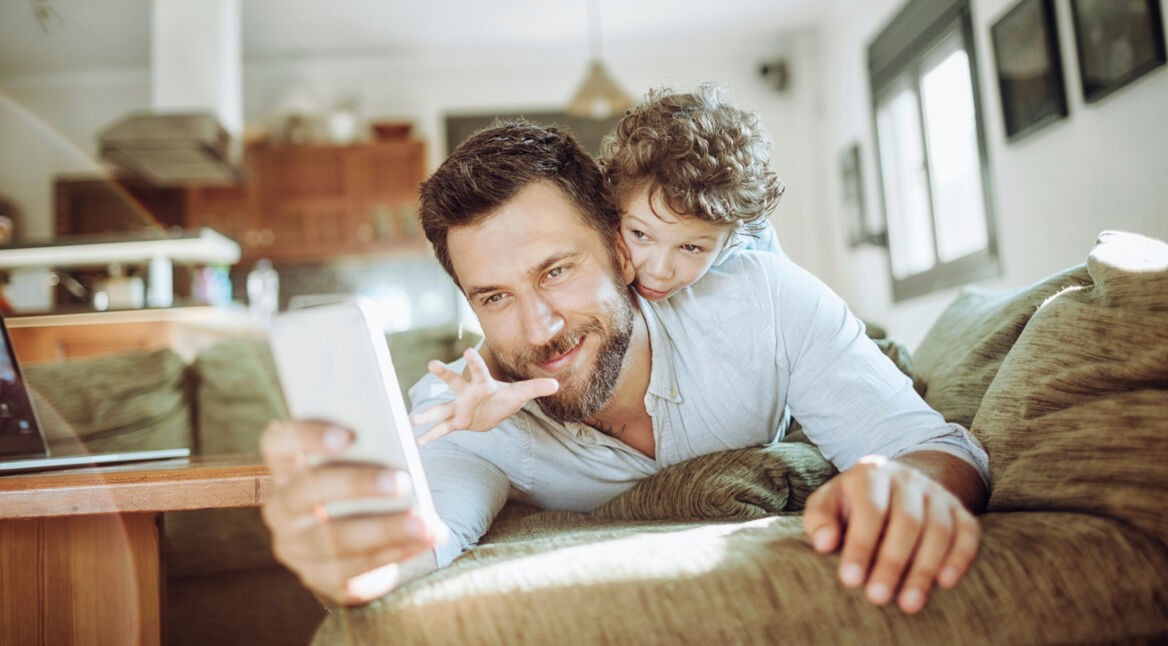 Ein junger Vater spielt mit seinem Sohn und hält ein Smartphone
