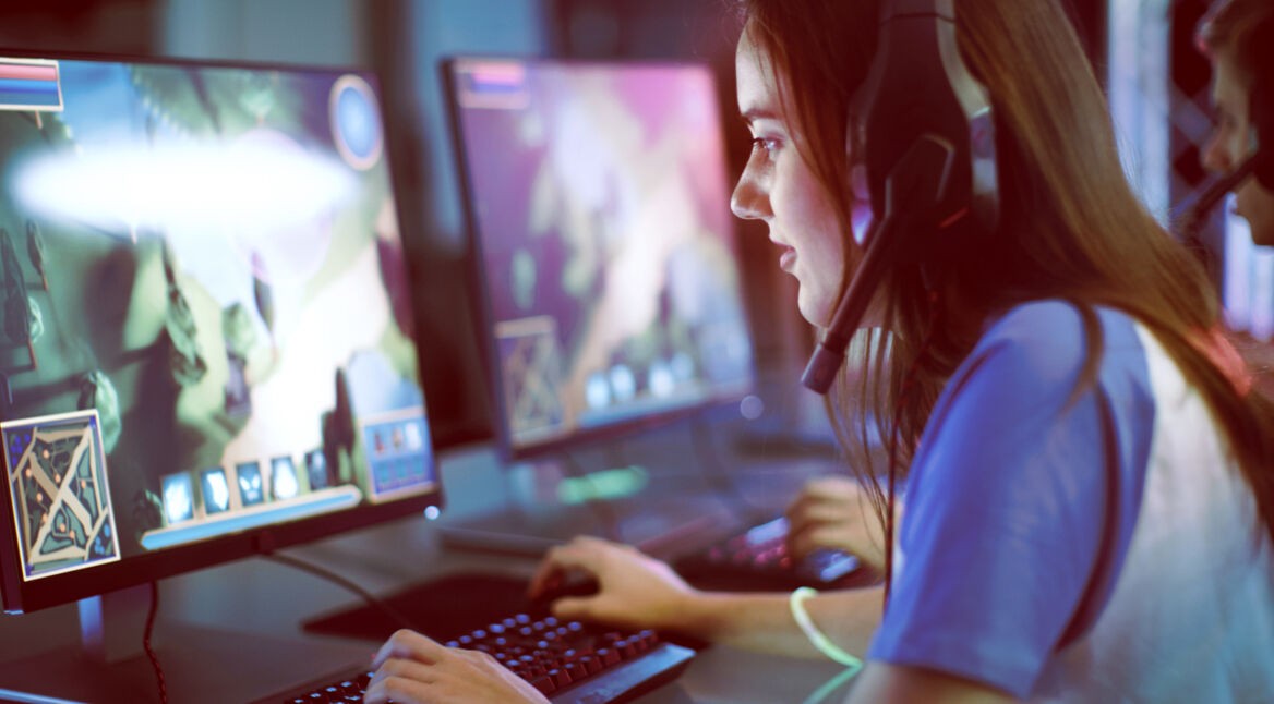 Professional Girl Gamer Plays in MMORPG/ Strategy Video Game on Her Computer. She's Participating in Online Cyber Games Tournament, Plays at Home, or in Internet Cafe. She Wears Gaming Headset.