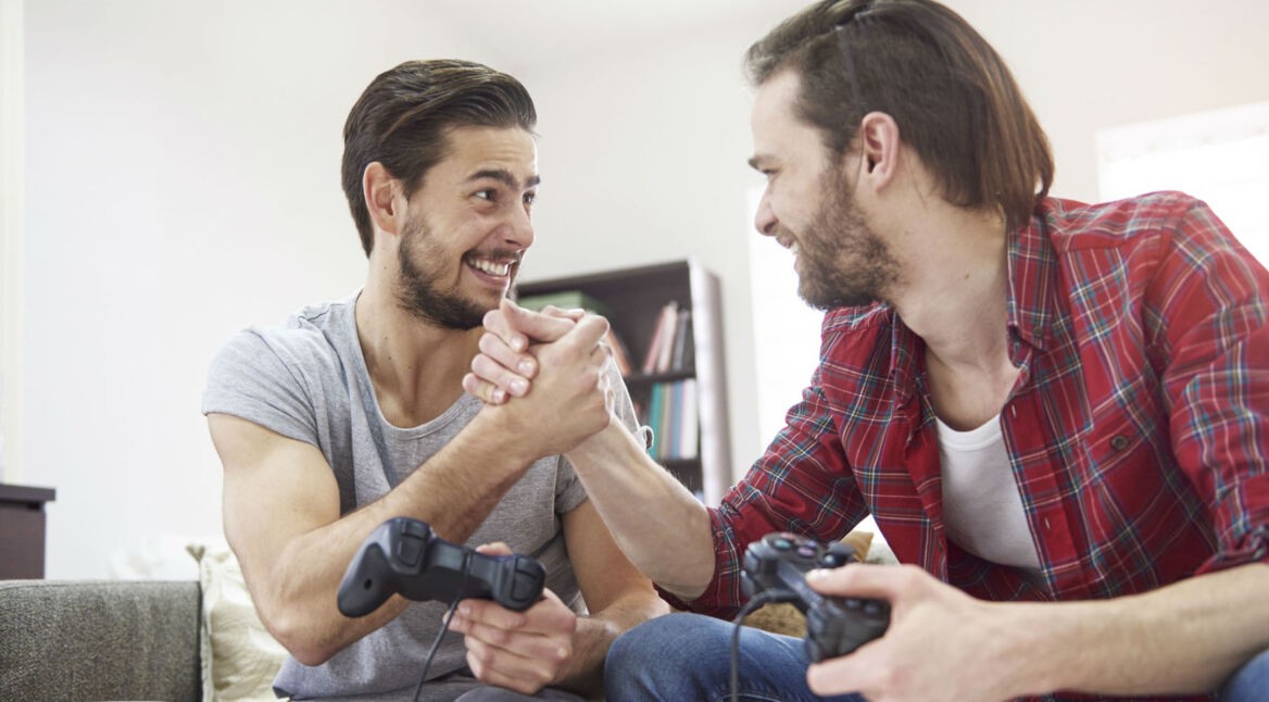 Zwei Freunde zocken mit ihren Controllern auf der Couch.