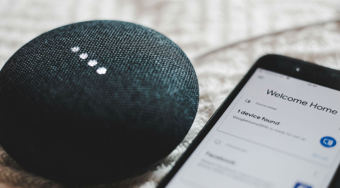 Schwarzer Google Home Mini liegt neben Smartphone.