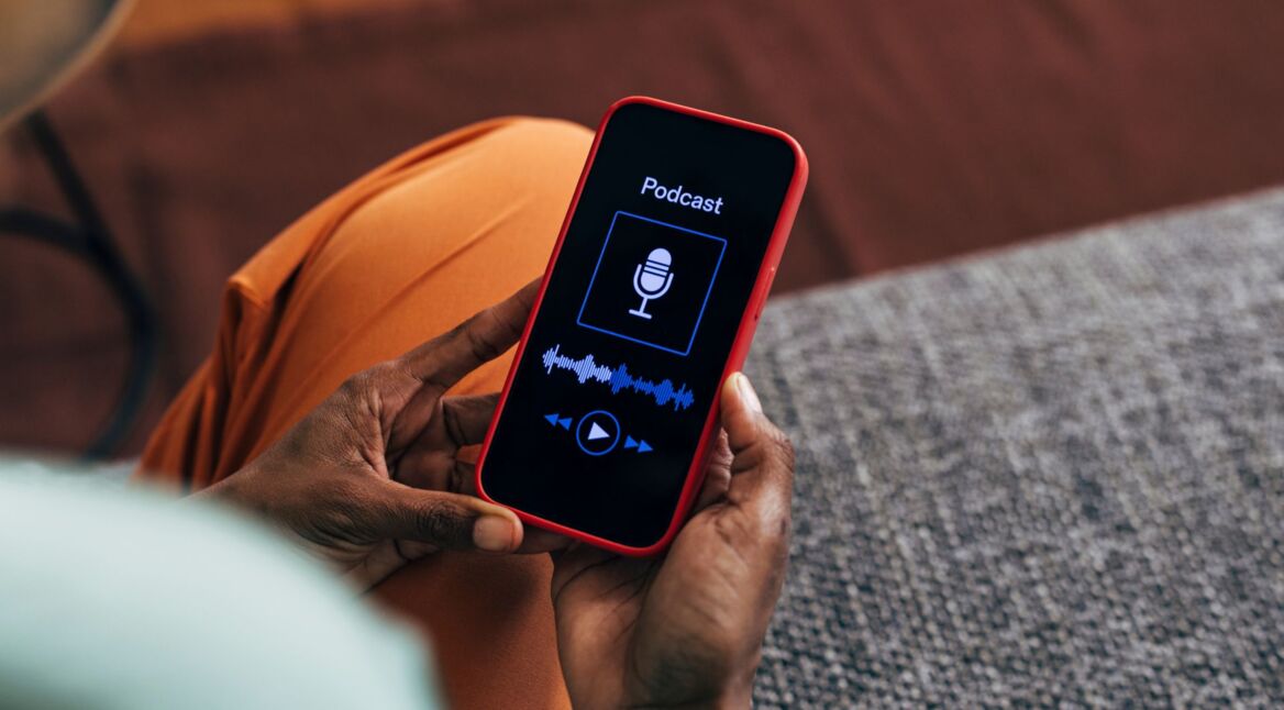 Person Holding Red Smartphone Displaying Podcast Screen Indoors