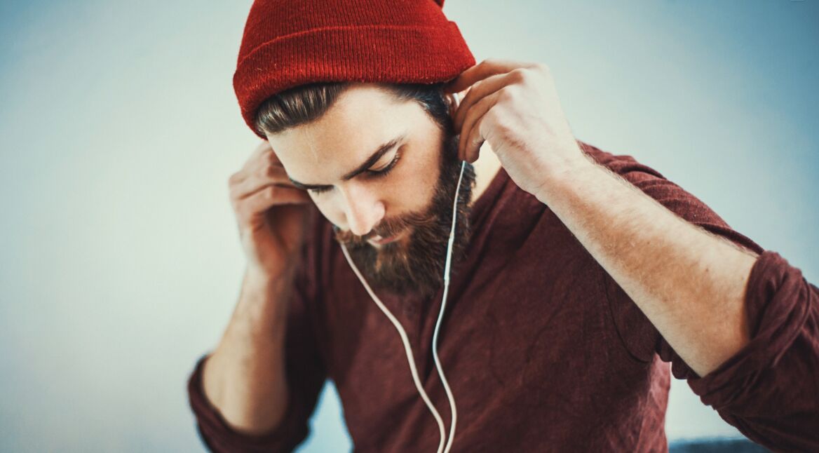 Junger Mann mit rotem Beanie hört einen Podcast auf Spotify