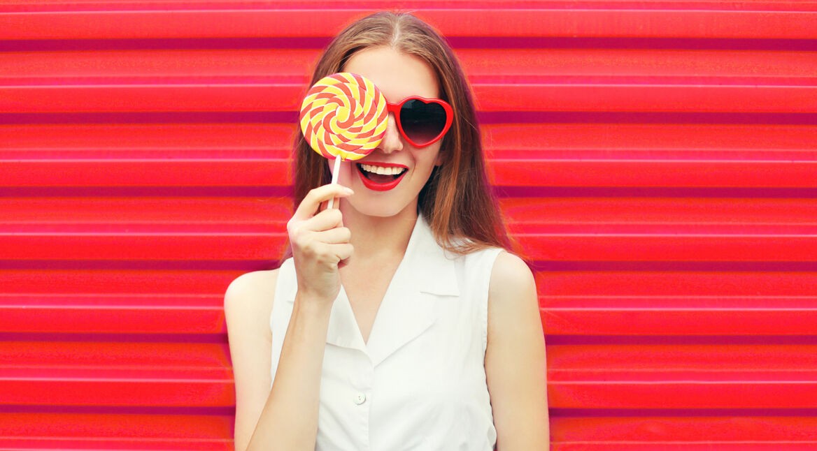 Sweet pretty young woman having fun with lollipop over pink