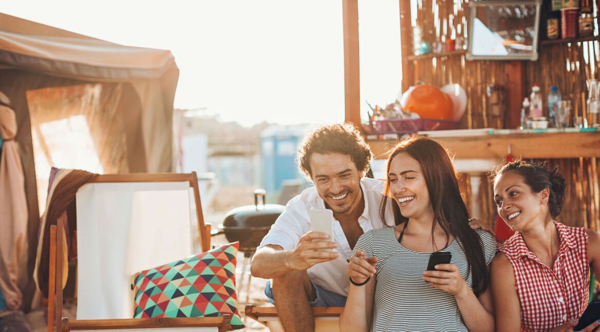 Freunde sitzen mit ihren Smartphones am Strand.