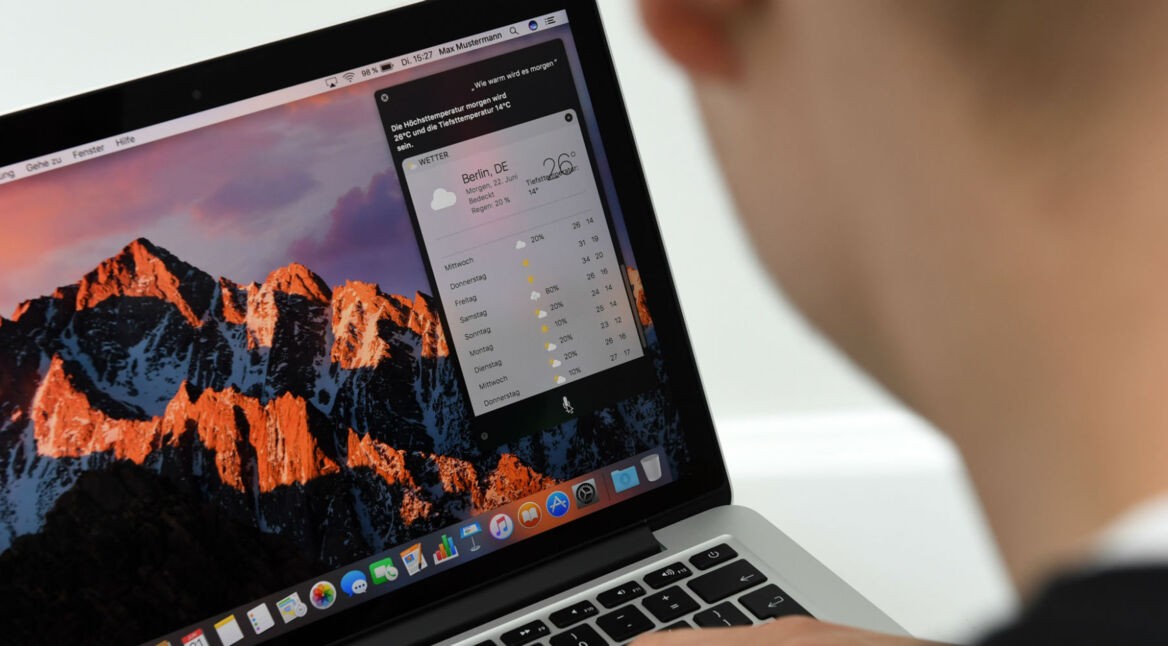 Junger Mann sitzt vor Mac-Computer.