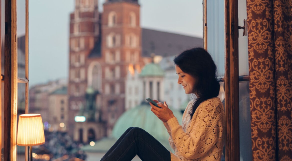 Junge Frau sitzt am Fenster und verwendet ihr Smartphone.