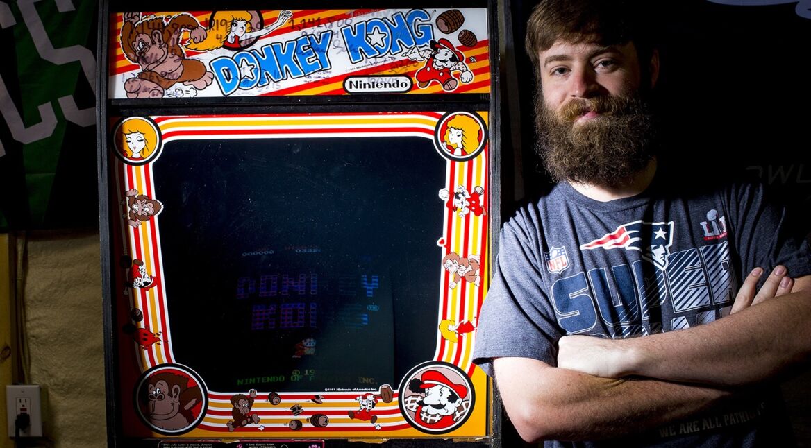 Ein Mann steht neben einem Donkey Kong Arcade-Spielautomaten
