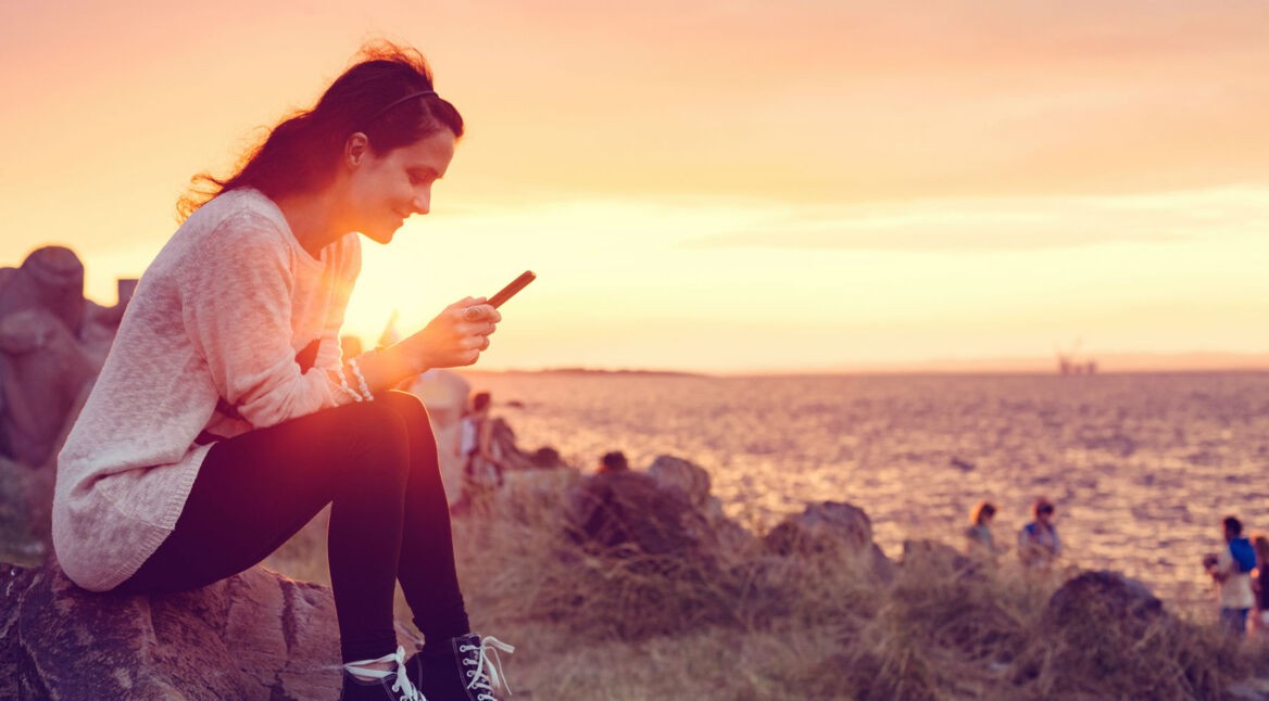 Junge Frau sitzt mit ihrem Smartphone am Strand.
