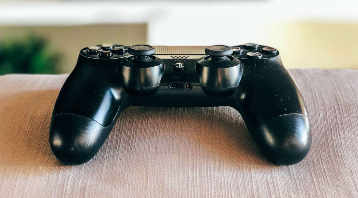 Schwarzer PS4-Controller liegt auf der Couch.