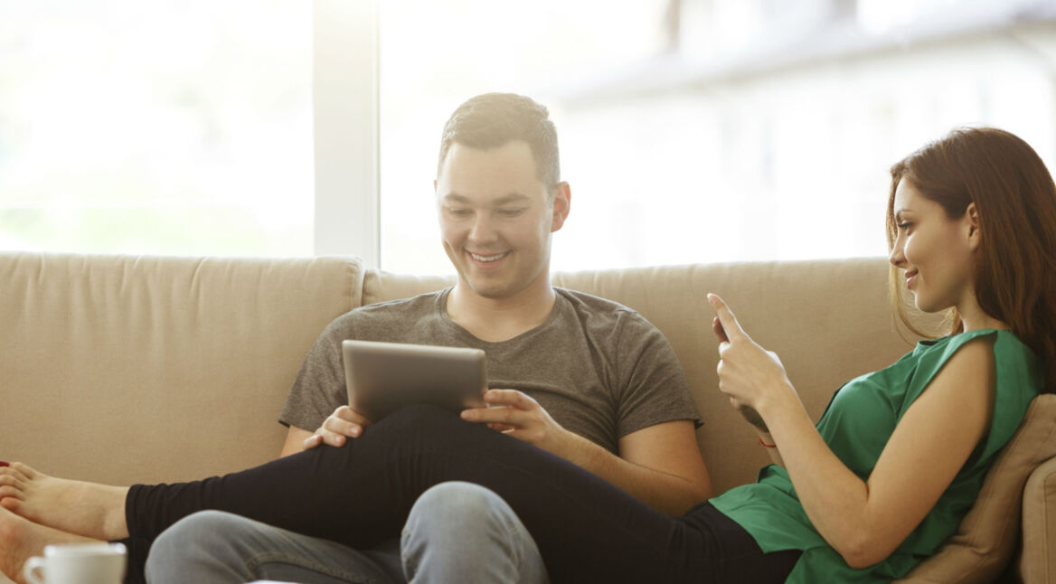 Junges Paar entspannt mit Smartphone und Tablet auf der Couch.