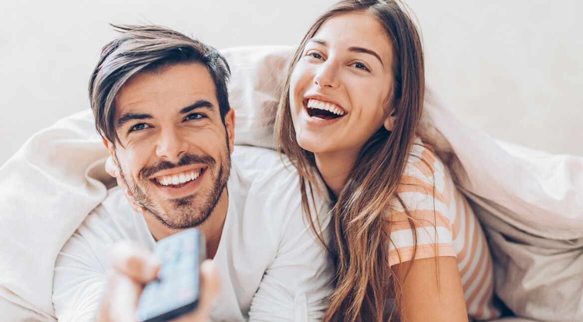 Ein junges Pärchen schaut im Bett liegend eine neue Serie