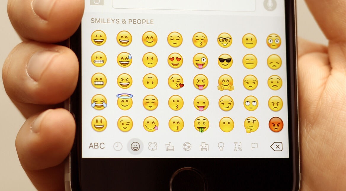 Ein junger Mann tippt eine Nachricht und nutzt dabei Emojis