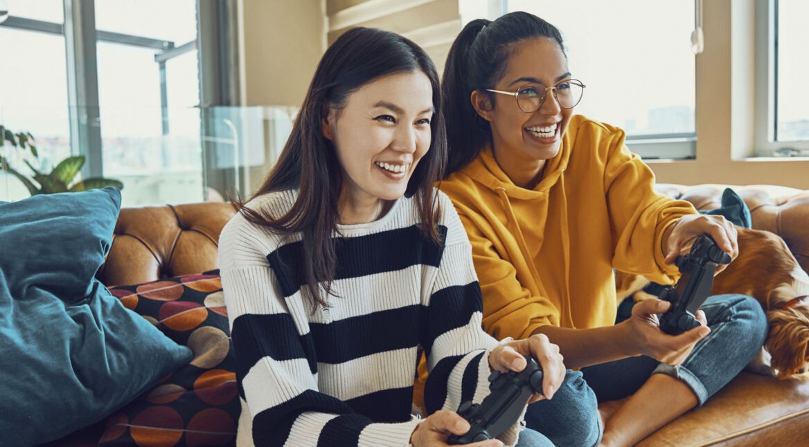 Zwei Freundinnen zocken mit ihren Controllern ein PS4-Spiel.