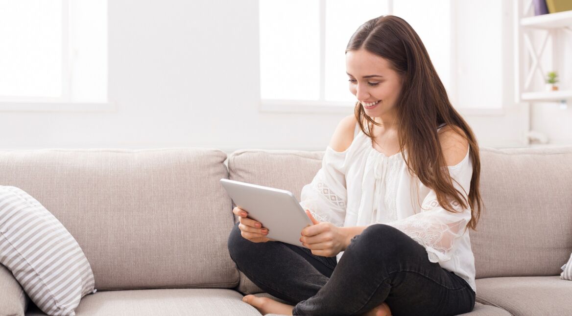 Junge Frau sitzt mit Tablet auf der Couch