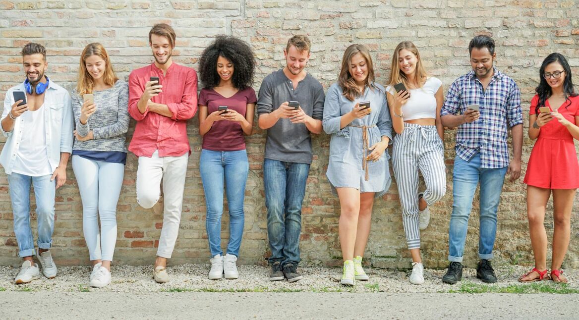 Diverse culture people using mobile smartphone outdoor - Happy friends having fun with technology trends - Youth, new generation addiction and friendship concept - Warm filter