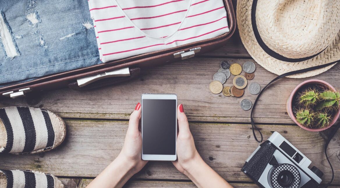 Travel preparations concept with suitcase, clothes and accessories on an old wooden table.