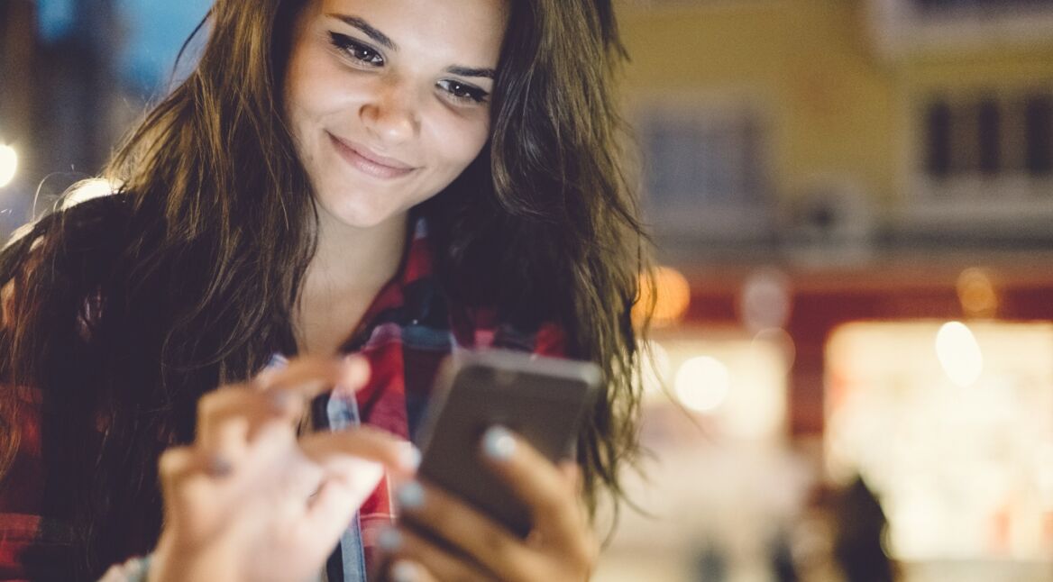 Eine junge Frau liest ihre WhatsApp-Nachrichten auf ihrem Smartphone