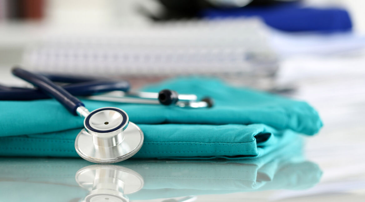 Medical stethoscope head lying on green doctor uniform