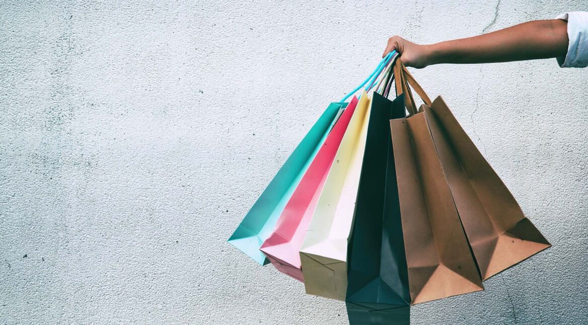 Closeup the colorful shopping bags were holding by lady hand,in front of grunge surface cement wall,in abstract art design,classic old film tone,blurry light around.