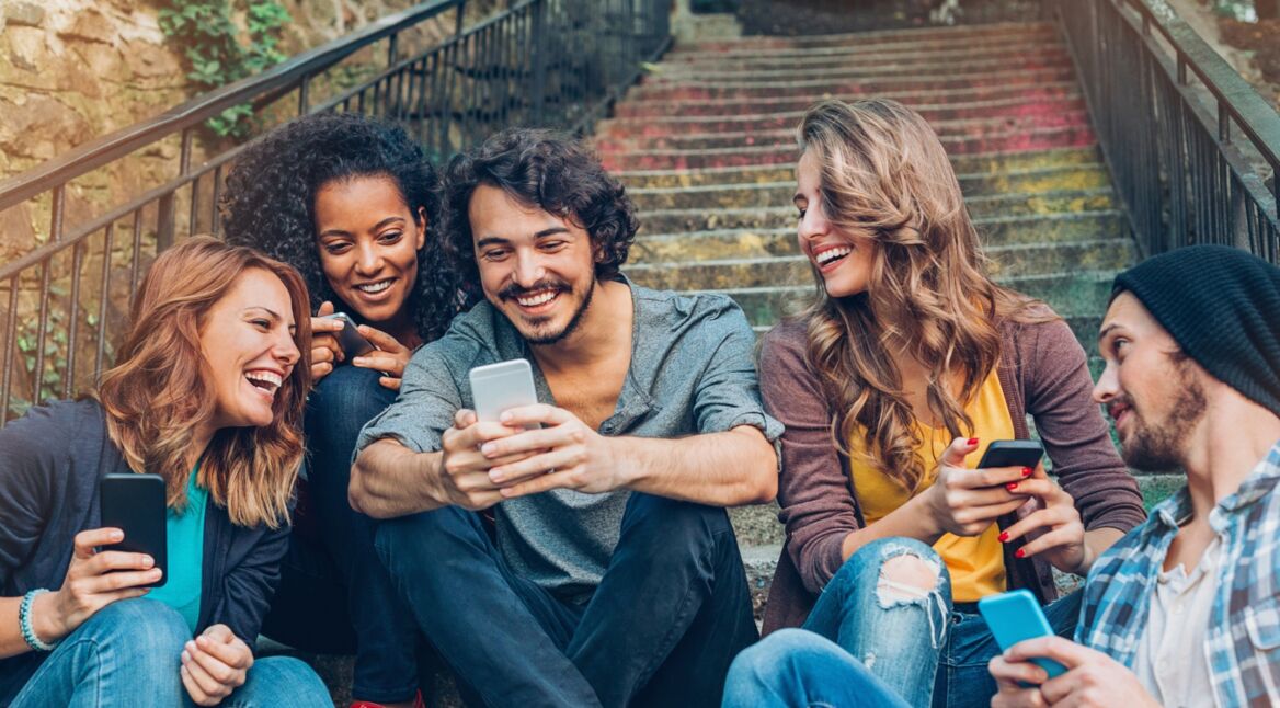 Junge Leute sitzen auf einer Treppe und schauen auf ein Smartphone