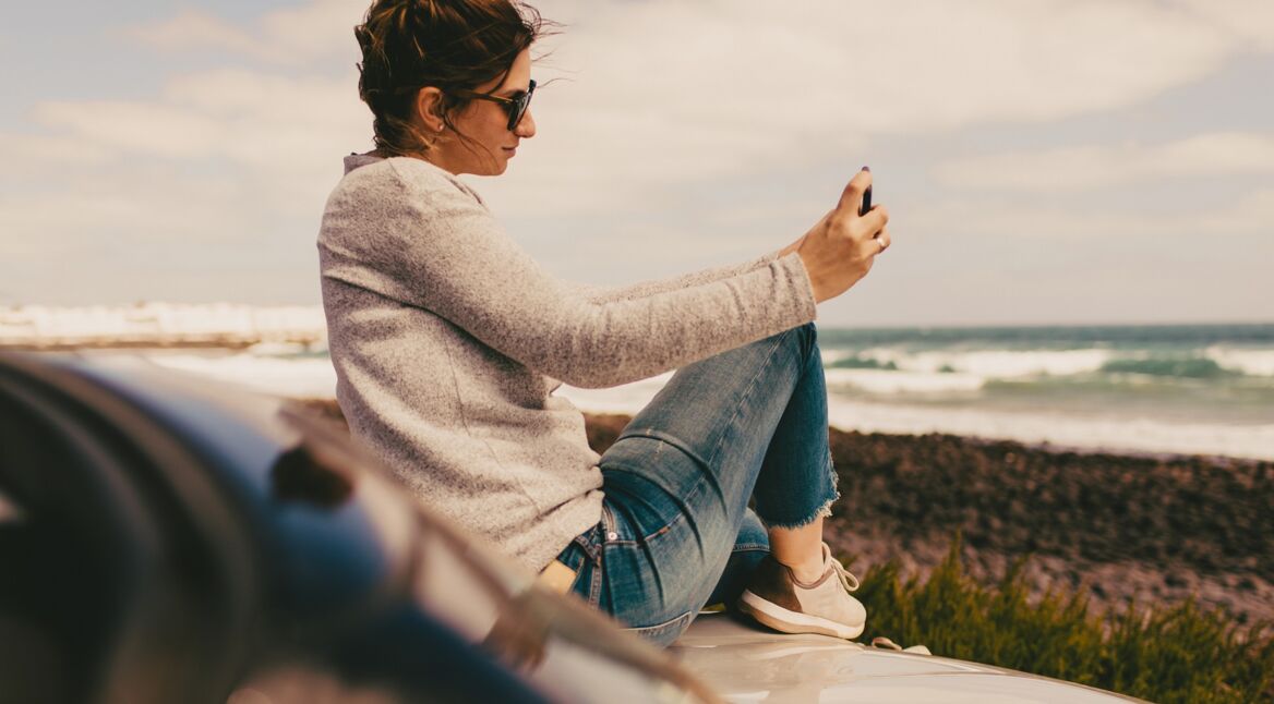 Eine junge Frau sitzt am Strand und installiert sich eine App
