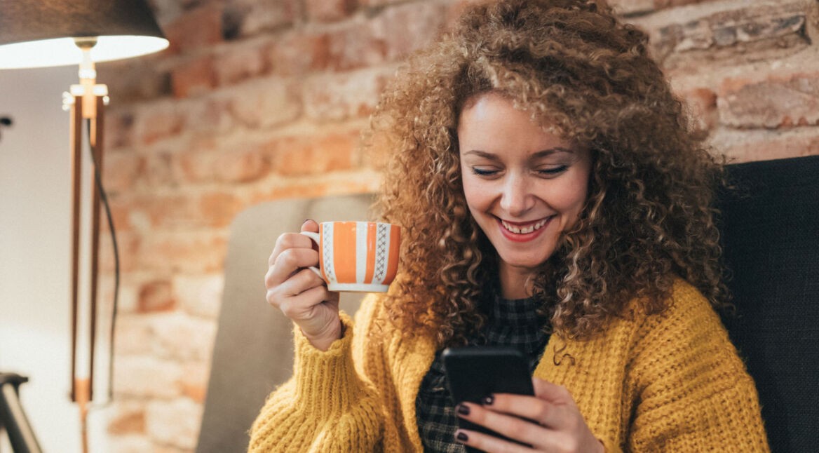 Junge Frau öffnet auf dem Smartphone ihre Alexa-App.