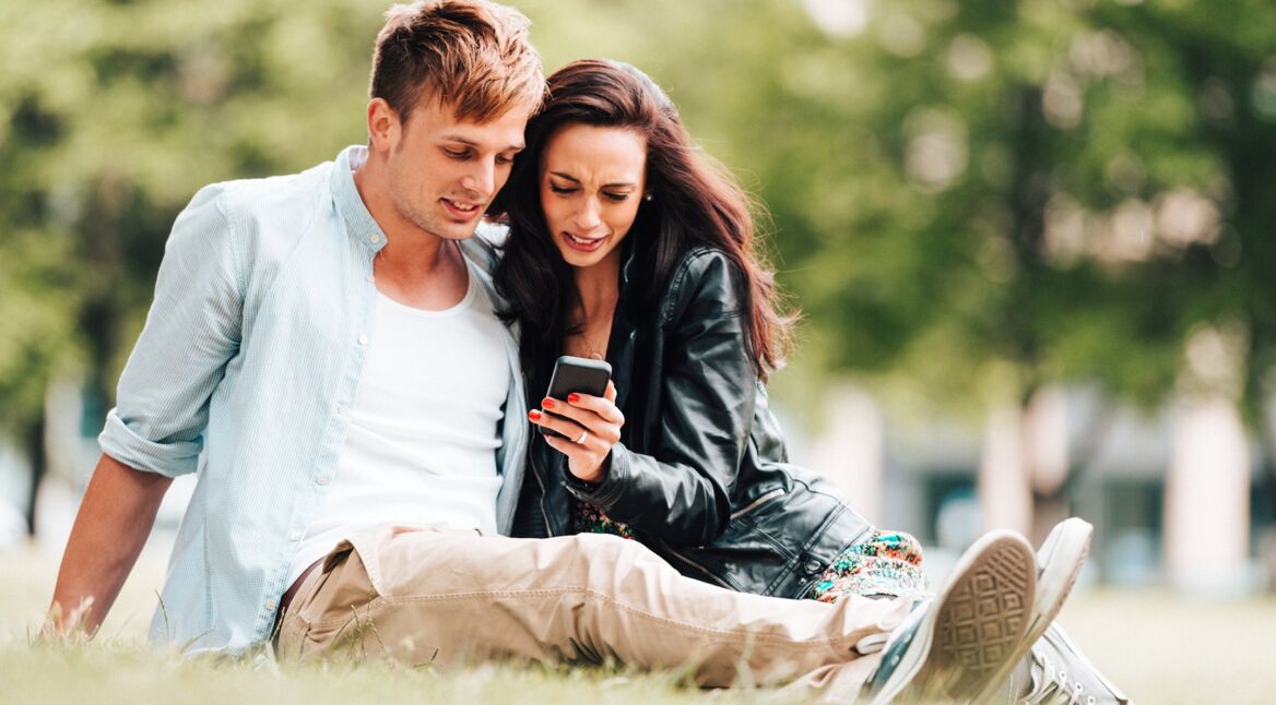 Junge Paar sitzt auf der Wiese mit iPhone