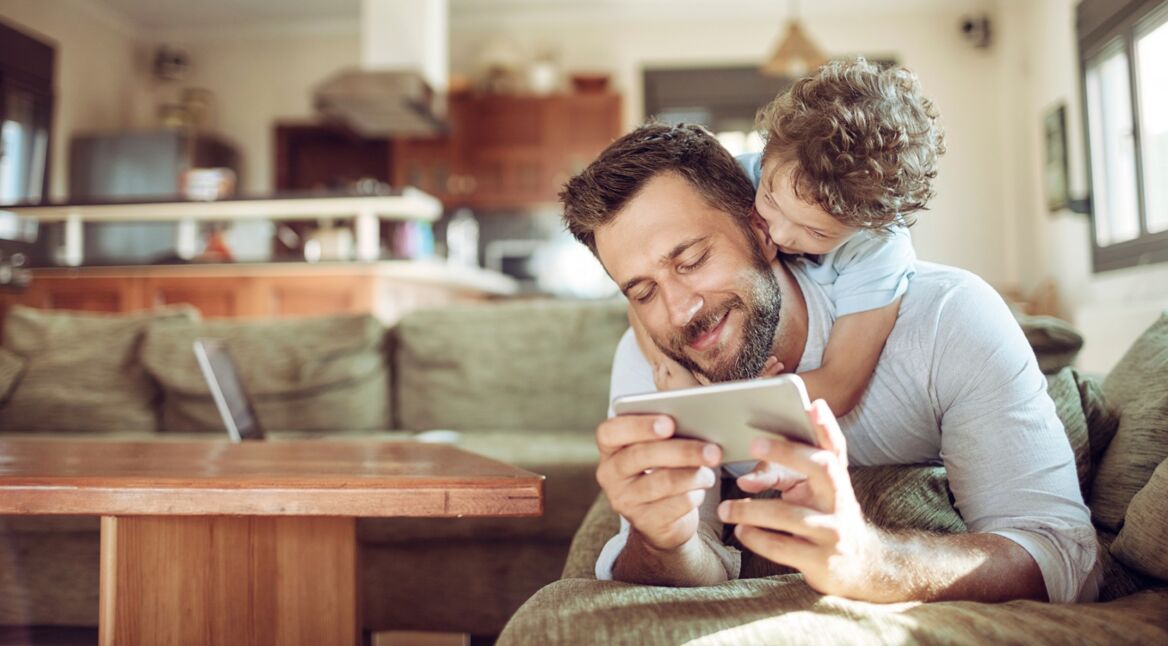 Ein junger Vater spielt eine Kartenspiel-App auf dem Smartphone