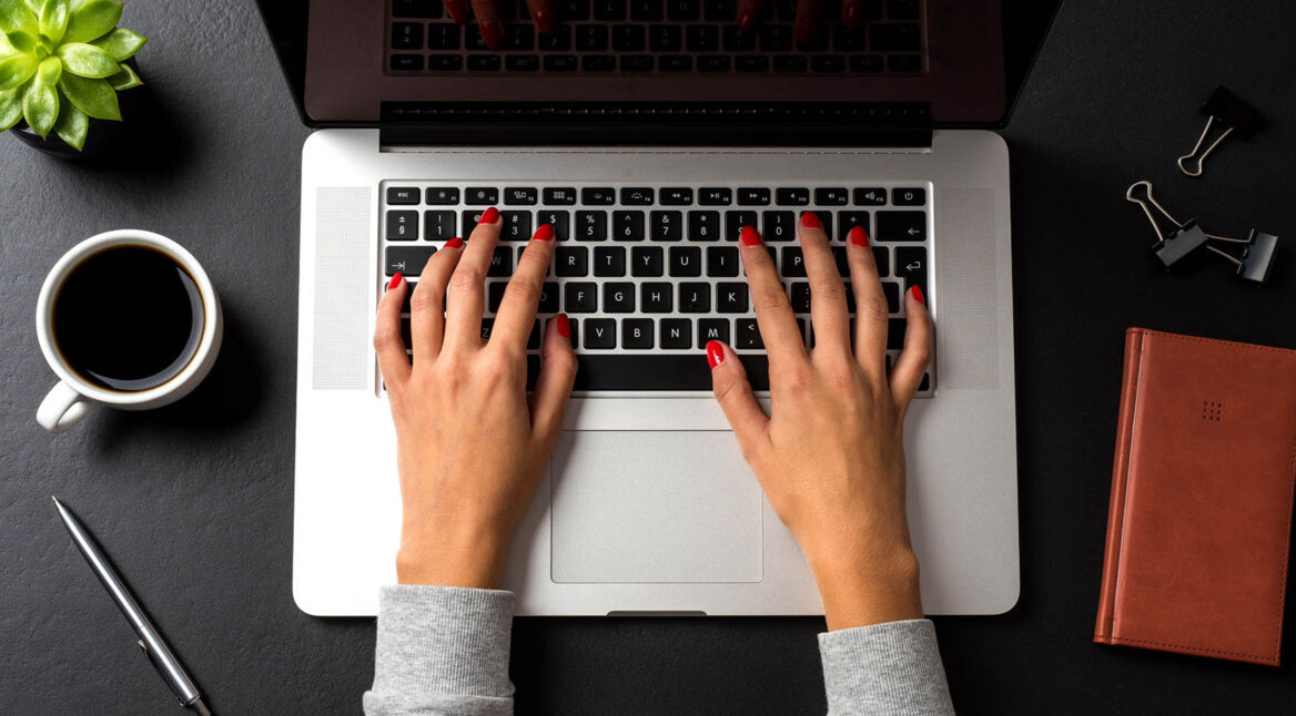Junge Frau tippt auf die Tastatur ihres MacBooks.