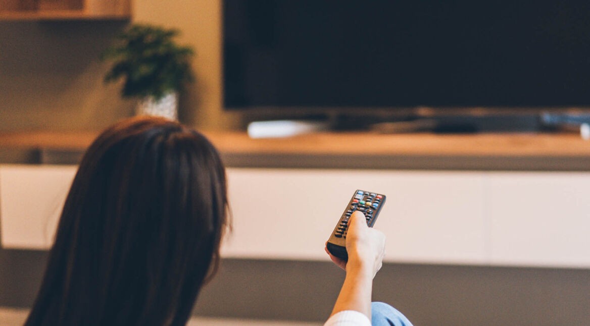 Junge Frau schaltet am TV die Audiodeskription von Netflix ein.