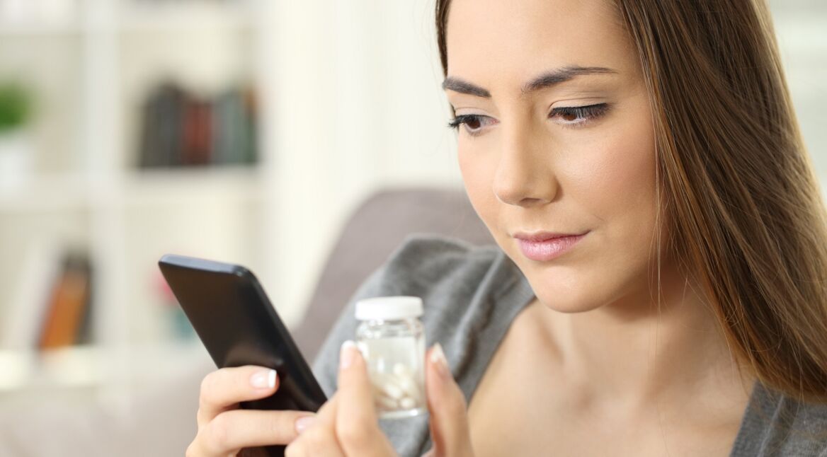 Eine Frau betrachtet Tabletten und ein Smartphone.