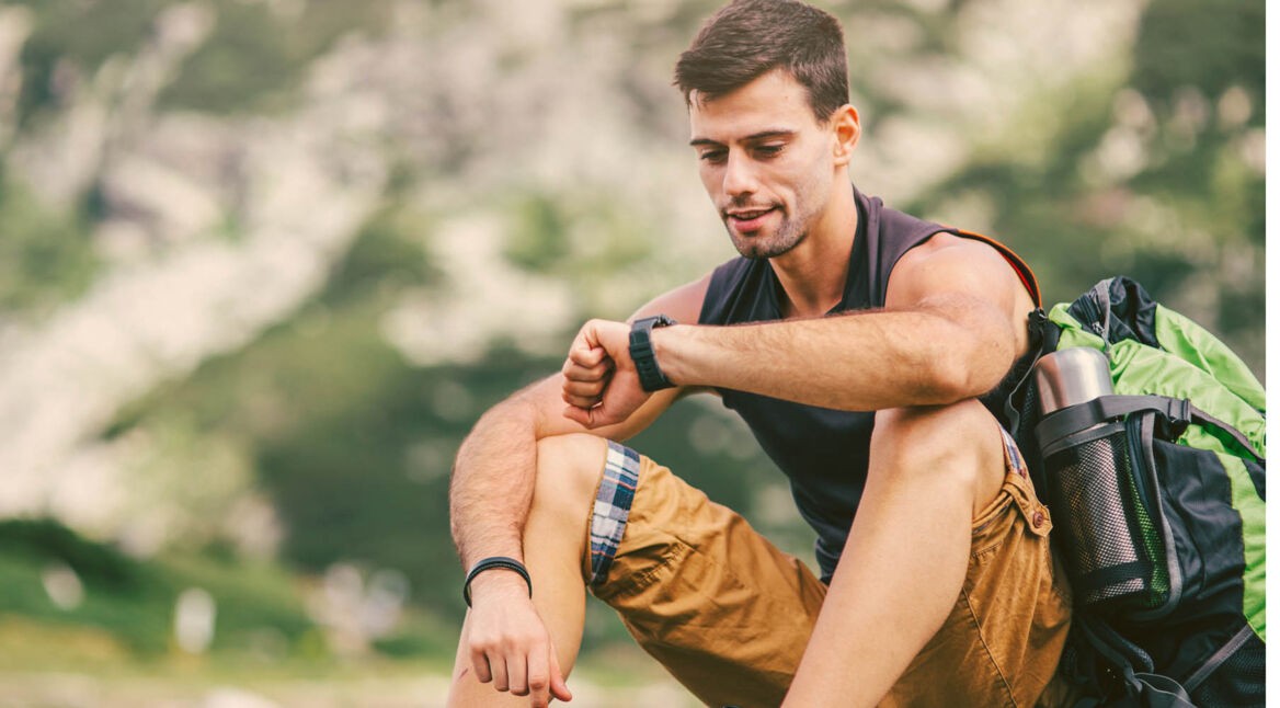 Junger Mann schaut beim Wandern auf seine Galaxy-Smartwatch.