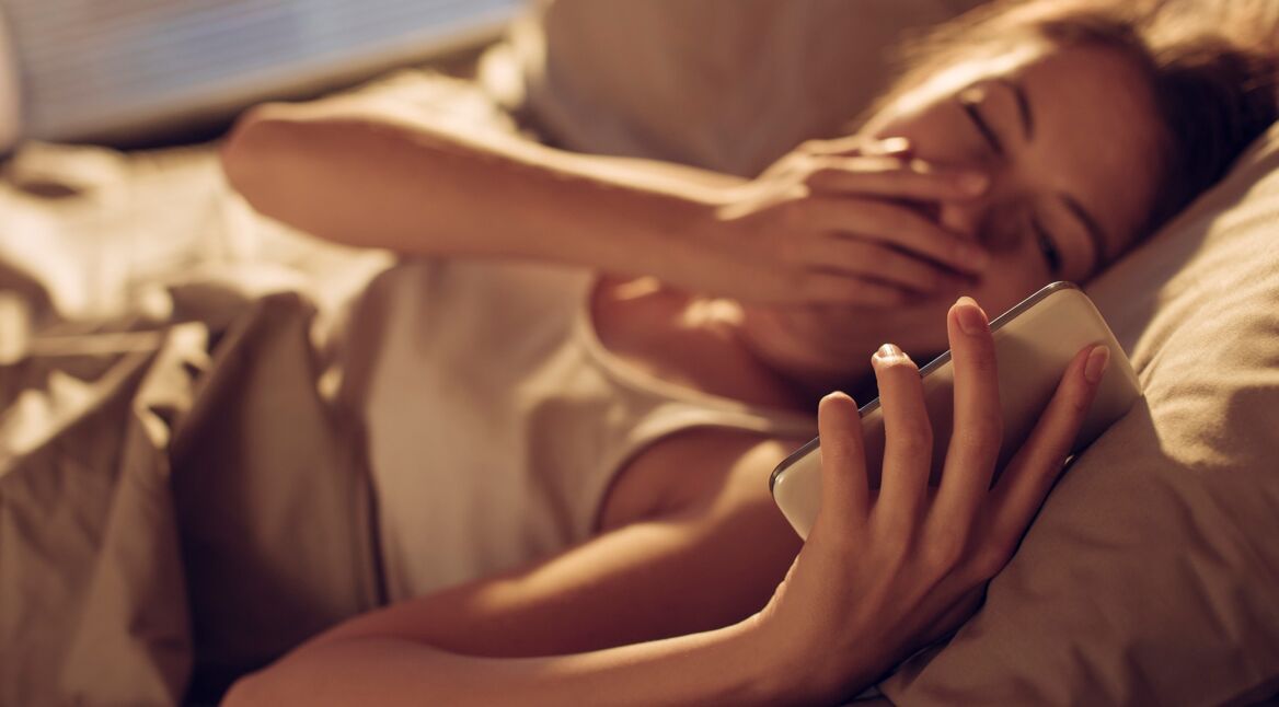 Junge Frau nutzt Uhren-App im Bett