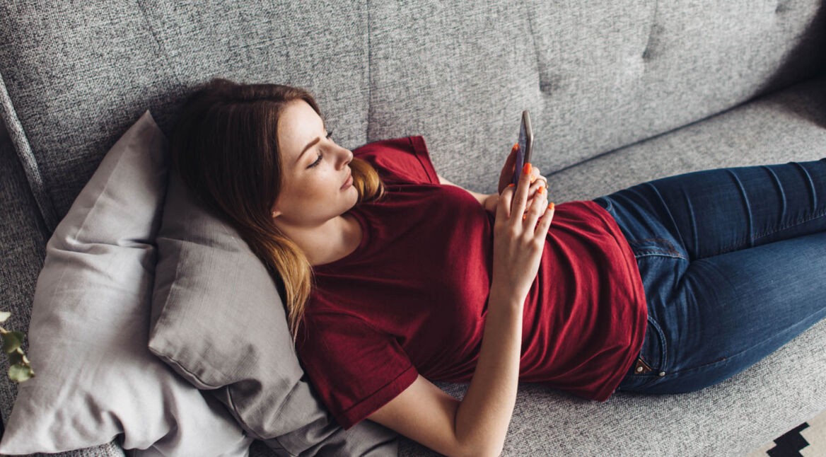 Junge Frau lädt Android 10 auf ihr Gerät, während sie auf dem Sofa liegt.