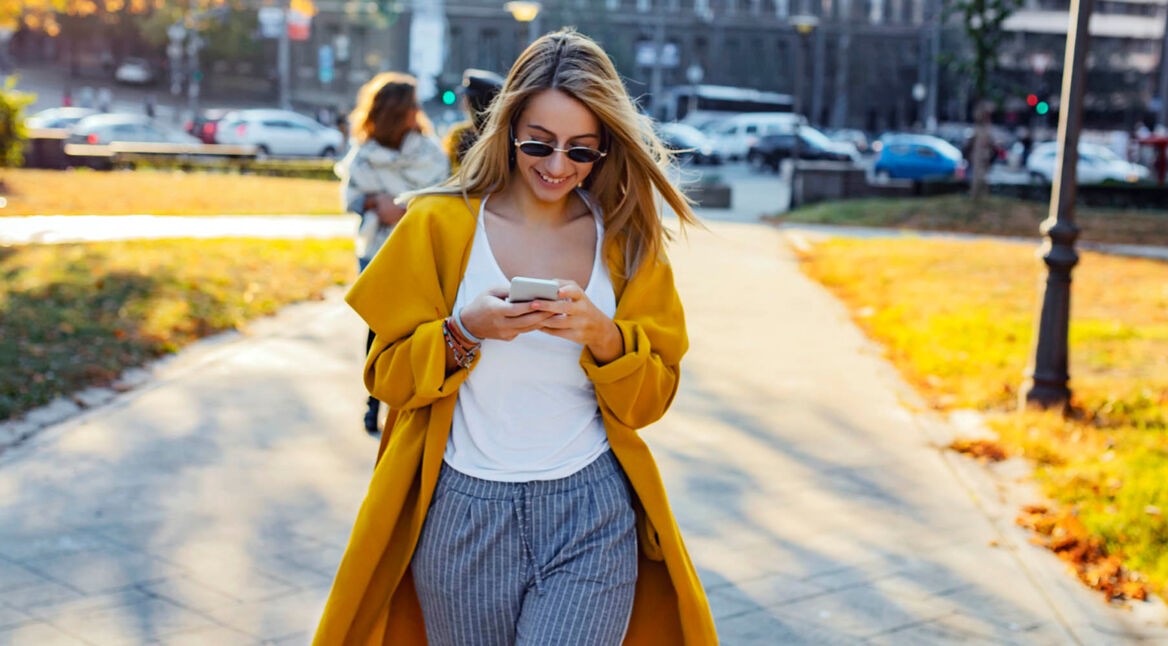 Frau richtet beim Spaziergang mit ihrem iPhone ein Profil für die Nachrichten-App ein.