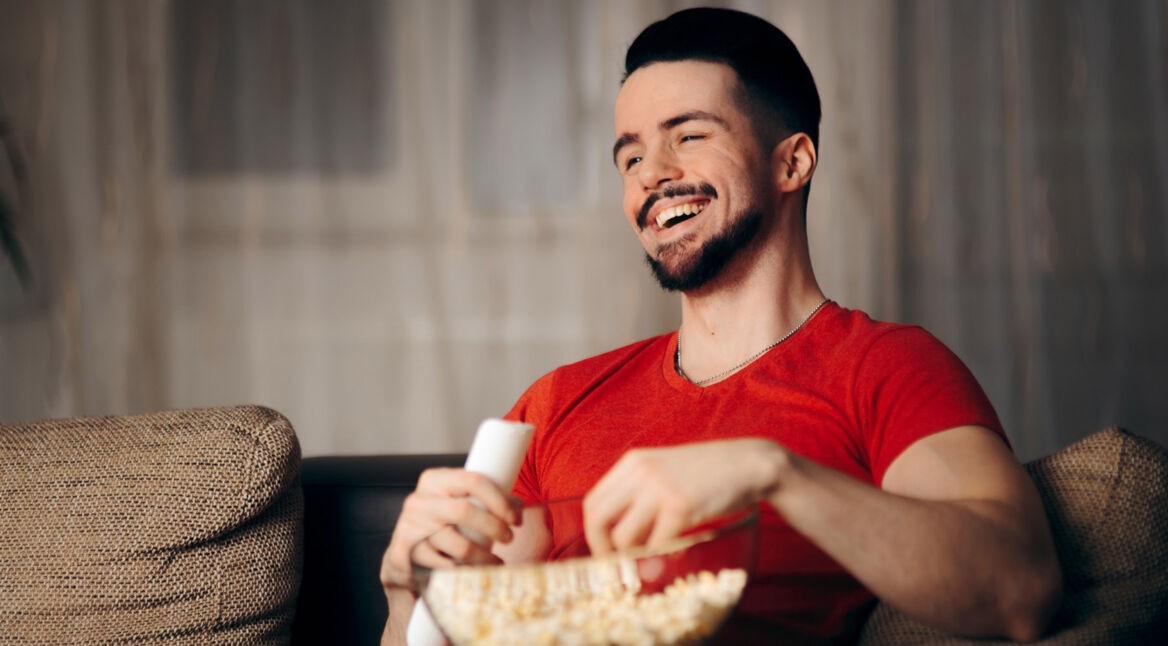 Junger Mann lächelt und nutzt Netflix ohne Probleme am Fernseher.