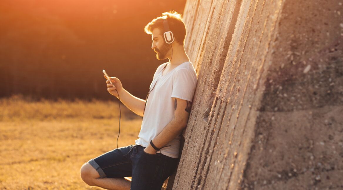 Junger Mann lehnt an einer Mauer und hört seine Lieblingsmusik.