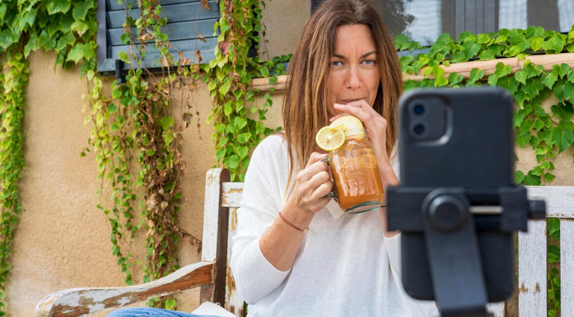 Eine junge Frau macht ein Selfie mit ihrem iPhone, das in einem Stativ vor ihr steht.
