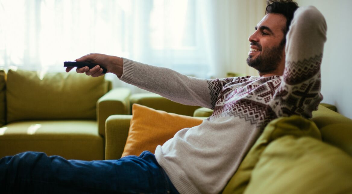 Junger Mann sitzt auf der Couch und schaut „He-Man and the Masters of the Universe“