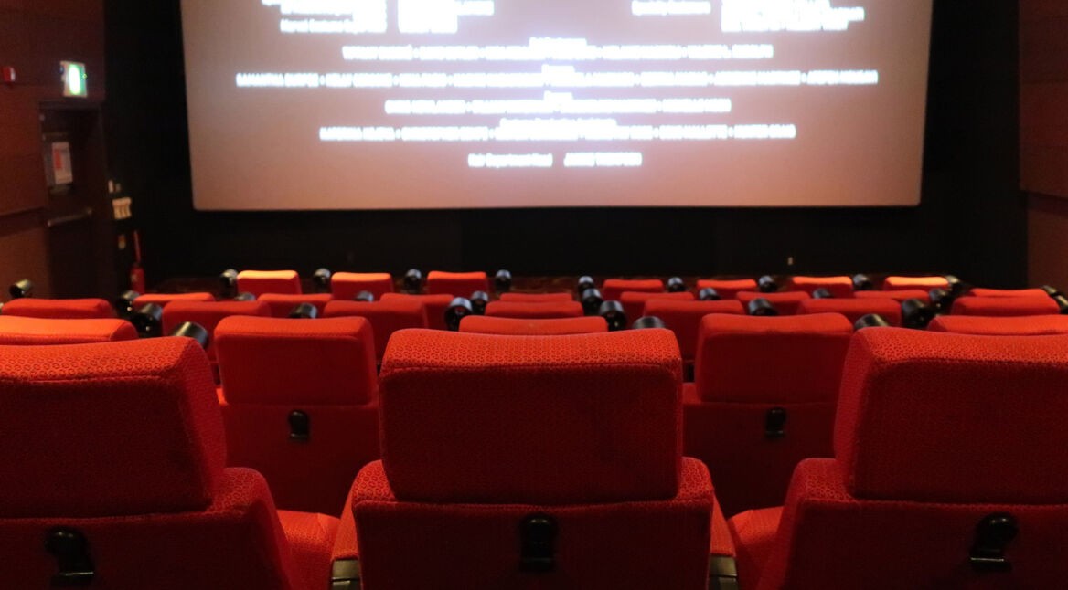 Rote Kinositze vor einer hellen Filmleinwand.