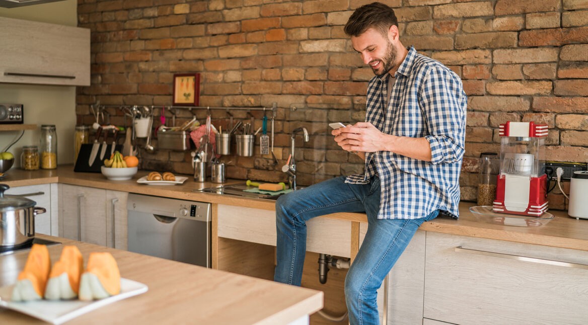 Ein Mann sitzt in der Küche und bedient ein Smartphone.
