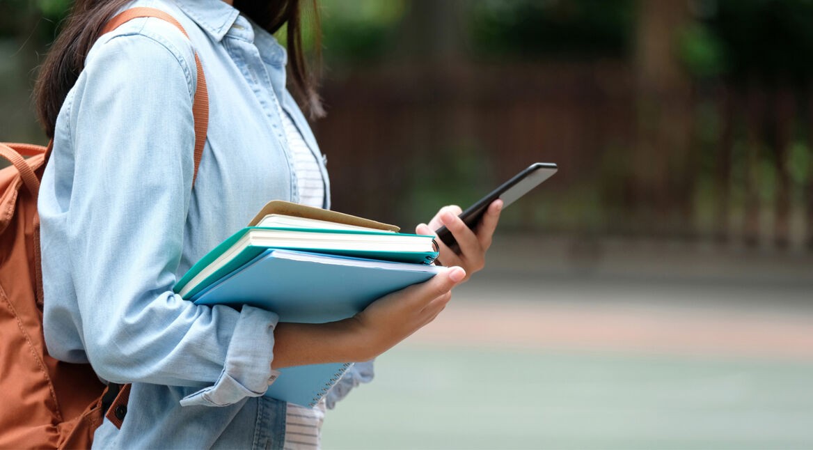 Schülerin mit Smartphone und Büchern