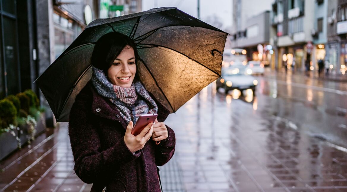 Frau informiert sich am Handy über das Wetter.