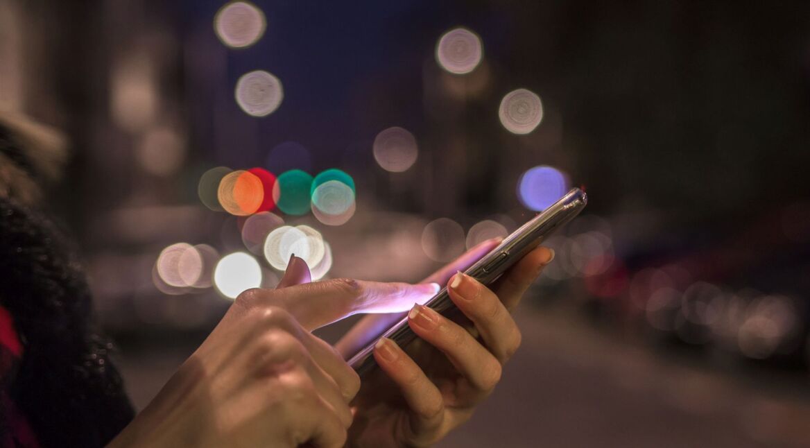 Frau nutzt nachts am Smartphone Google Maps im dunklen Design.