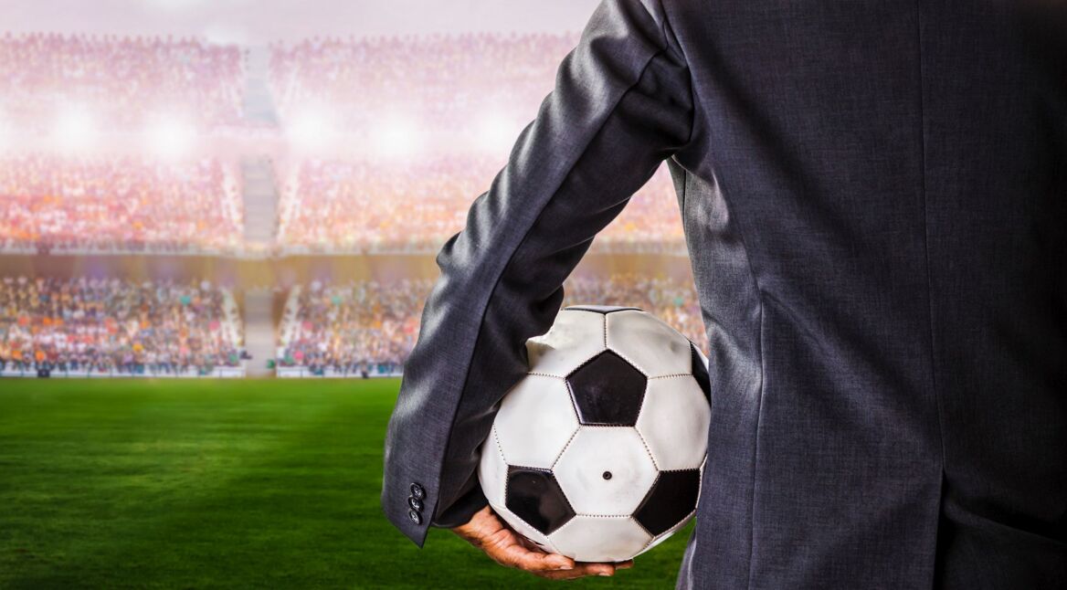 Fußballmanager steht am Spielfeldrand mit Ball im Arm.