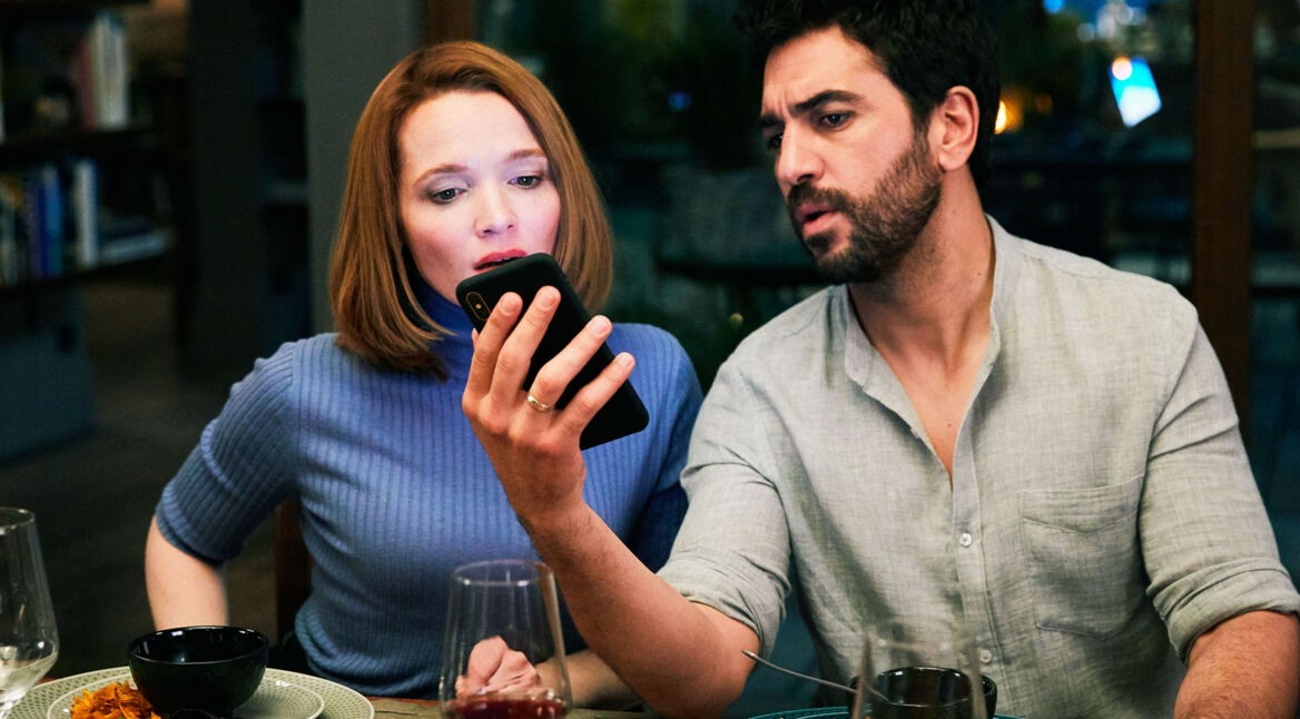 Elyas M'Barek zeigt Caroline Herfurth in "Das perfekte Geheimnis" etwas auf einem Smartphone. Foto: Constantin Film