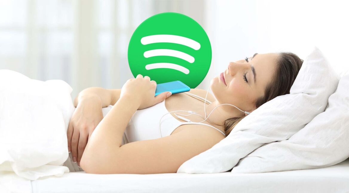 Frau liegt im Bett und hört übers Smartphone Spotify zum Einschlafen