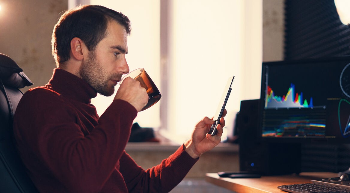 Mann mit Kaffeetasse in der Hand schaut auf sein iPad