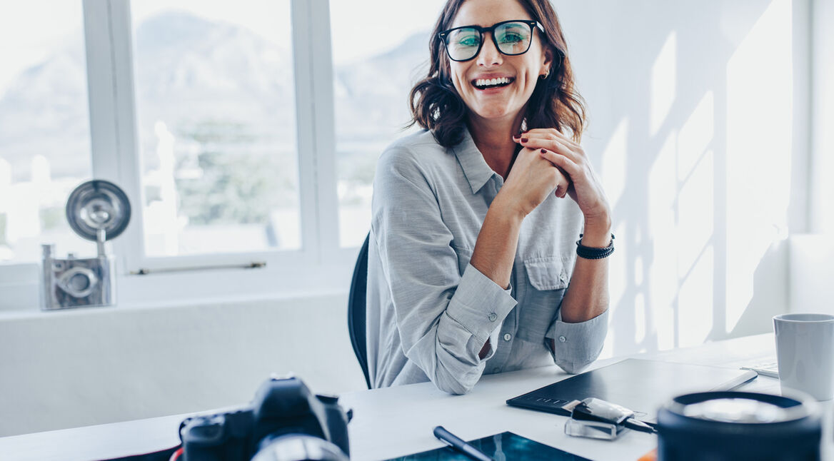 Eine Frau sitzt an einem Bürotisch und lacht