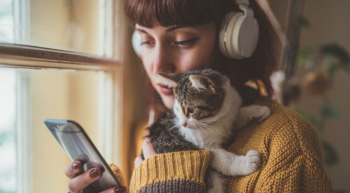 Frau hält Katze im Arm und hört mit ihrem Android-11-Handy Musik.
